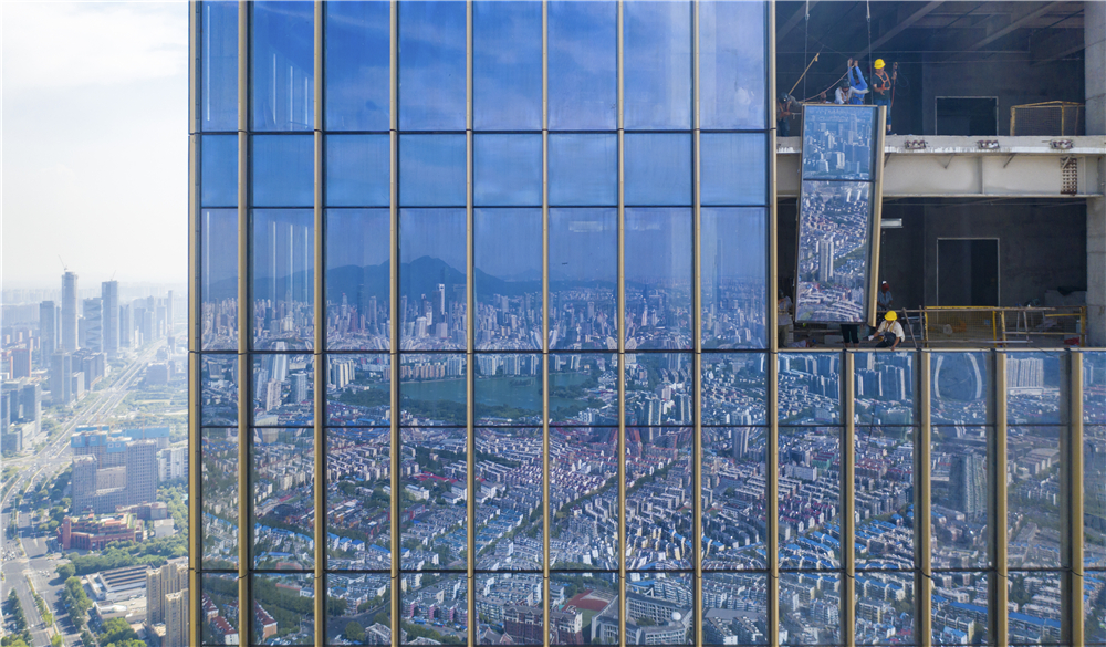 《城市拼图》方飞，2019.07 正在建设的摩天大楼在安装最后最快玻璃幕墙，玻璃幕墙里倒映出南京主城，而这些也都是建筑工人们用一砖一瓦堆砌而成.jpg